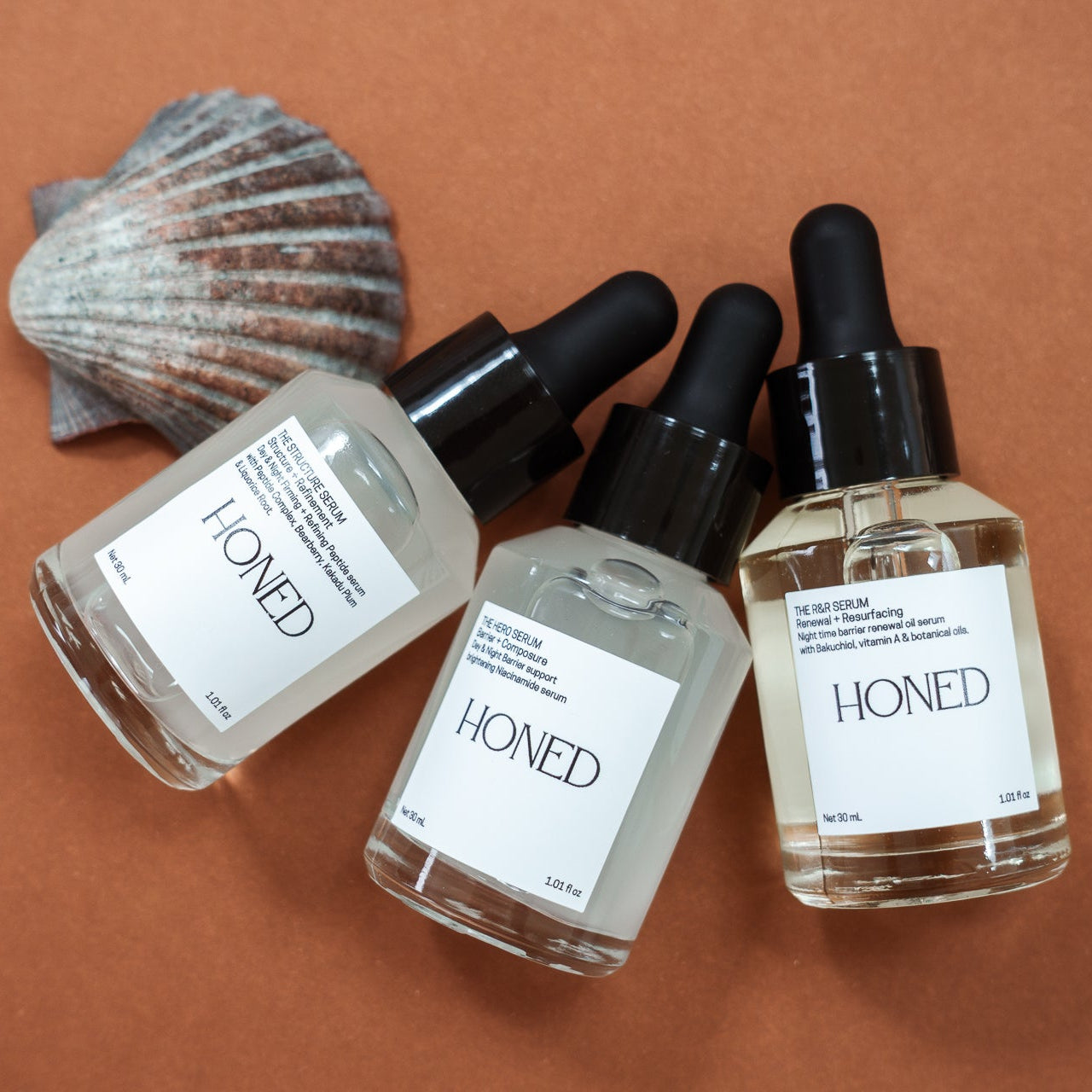 Peptide, niacinamide and bakuchiol serum Honed skincare bottles with a scallop shell on a brown background