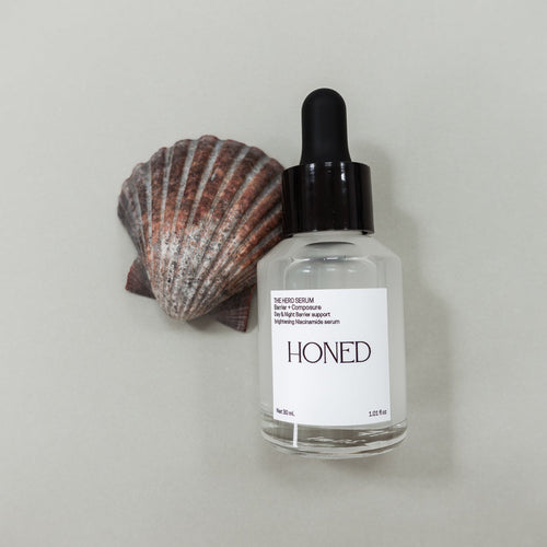 Bottle of 'Honed' niacinamide skincare serum with a scallop shell on a light gray background