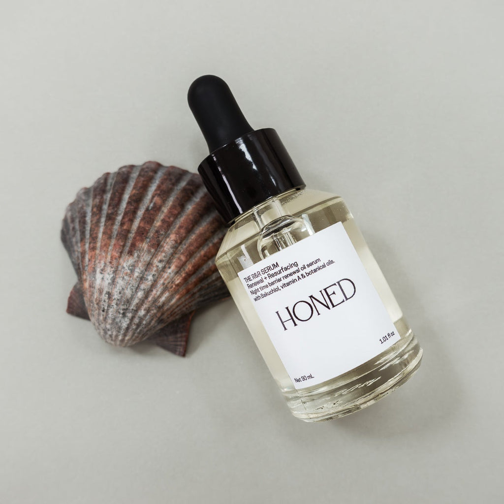 Bottle of 'Honed' renewal and resurfacing skincare serum with a scallop shell on a light gray background