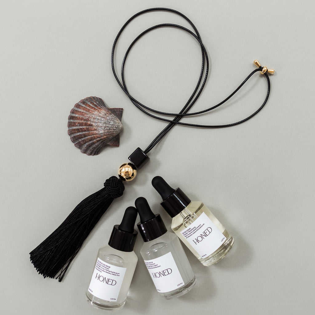 Set of three serums in dropper bottles with tassels and a shell on a gray background